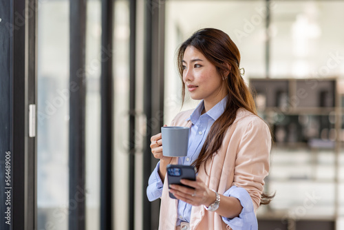 Portrait of a charming young woman businessman in the office standing holding a Coffee cup in hand and looking away from camera 