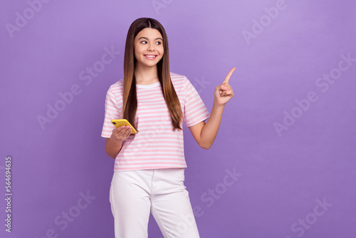 Photo of pretty dreamy lady wear striped white t-shirt chatting gadget looking pointing empty space isolated violet color background