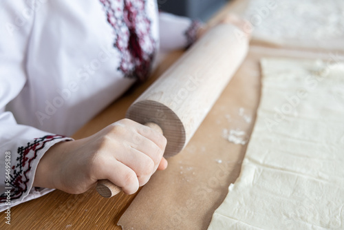 A girl in a Ukrainian national shirt rolls dough with a rolling pin