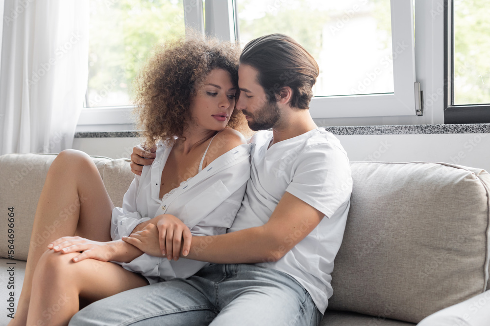 passionate man sitting on couch and hugging sensual woman in white shirt.
