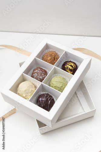 Healthy handmade chocolate candies in white box on white background. Six cheese truffles and packing tape. Sweet gift. Soft focus