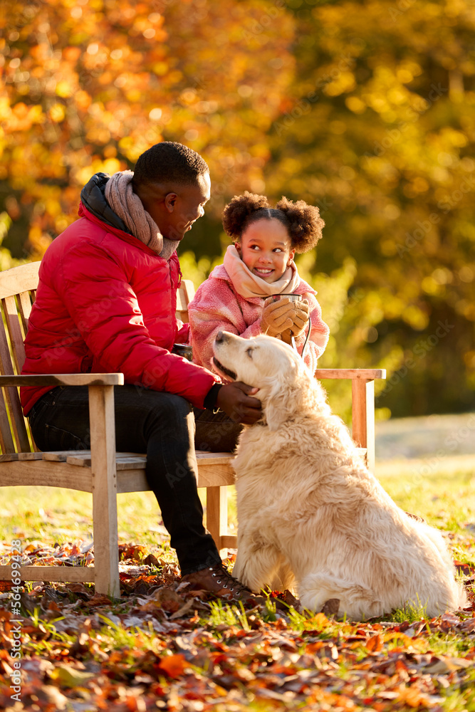 Fototapeta premium Father And Daughter With Hot Drink Sitting On Bench With Pet Dog On Walk In Autumn Countryside