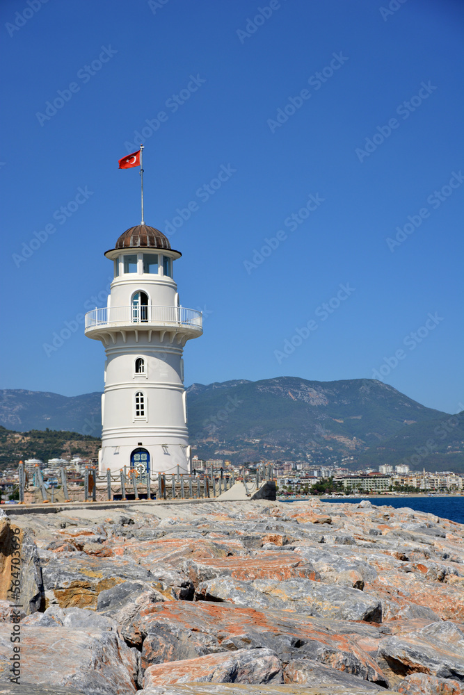 white lighthouse isolated with stony path, clear blue sky and mountains on background