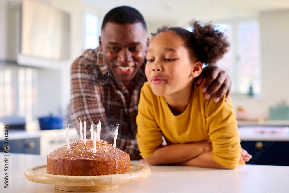 Father And Daughter At Home In Kitchen Celebrating Blowing Out Candles On Homemade Birthday Cake