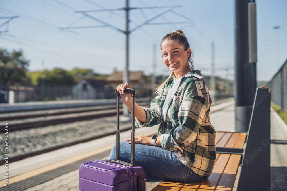 Happy woman enjoys sitting on a bench at the train station.	