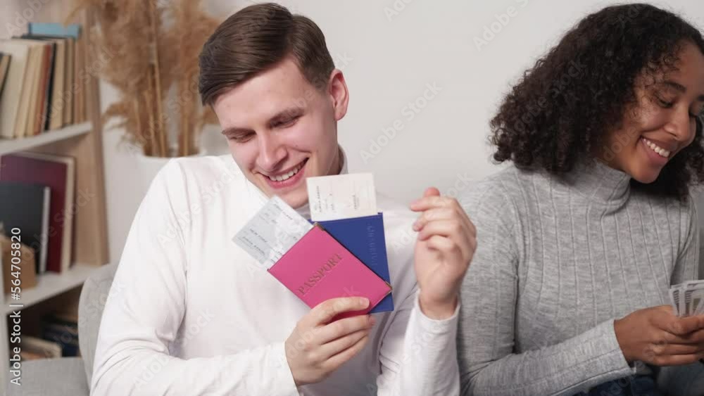 Vacation celebration. Excited couple. Travel joy. Happy beloved man and woman dancing sitting sofa with passport tickets cash dollars in light room interior. Vacation celebration. Excited couple. Travel joy. Happy beloved man and woman dancing sitting sofa with passport tickets cash dollars in light room interior.