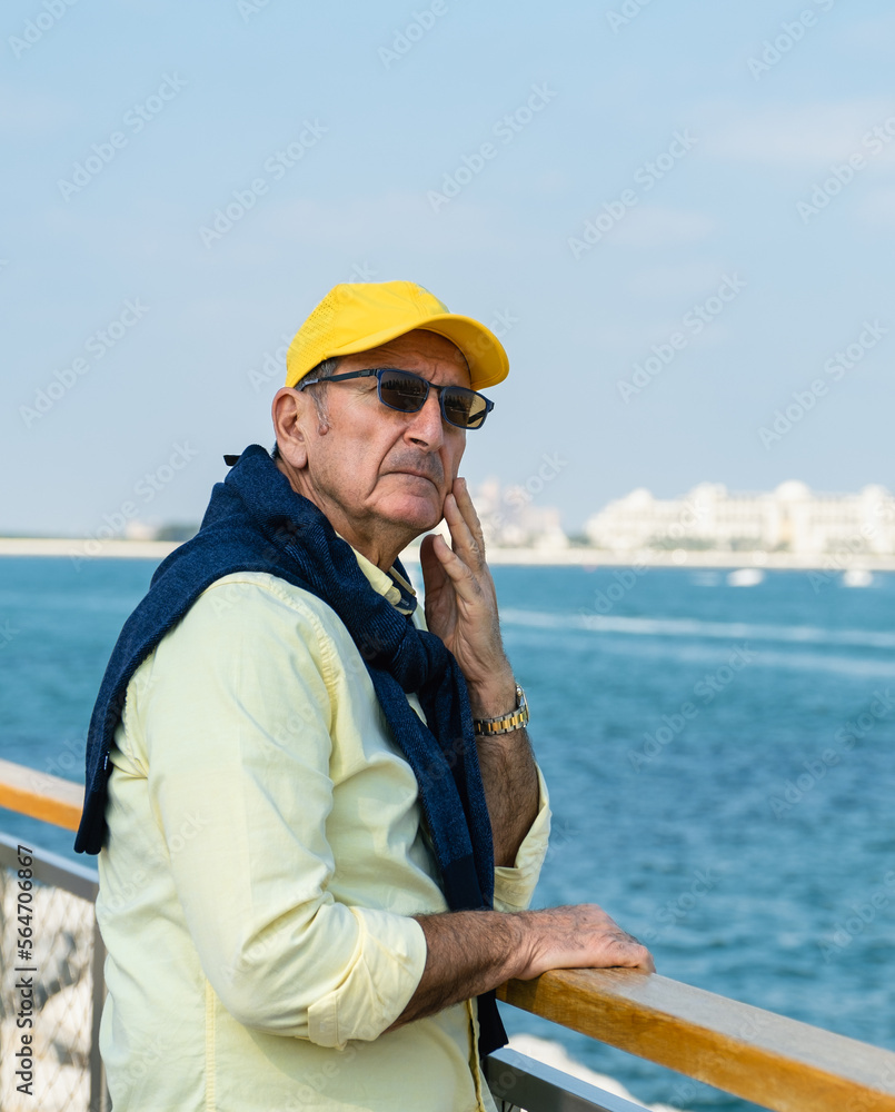 Thoughtful senior man walking along a promenade alongside a marina