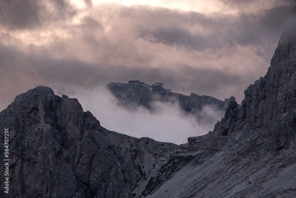 A mountain refuge in the italian dolomites alps surrounded by low clouds at dusk