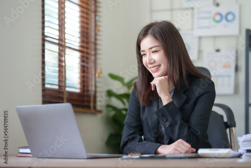 Smiling and attractive asian businesswoman enjoying working using laptop computer at office. © amnaj