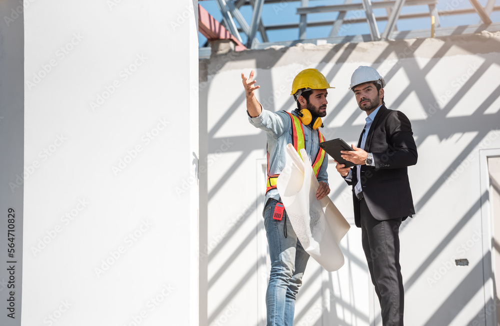 Teamwork men in construction site, Two civil engineer in safety helmet hard hat using digital tablet and blueprint working while standing at factory. Teamwork men in construction site, Two civil engineer in safety helmet hard hat using digital tablet and blueprint working while standing at factory.