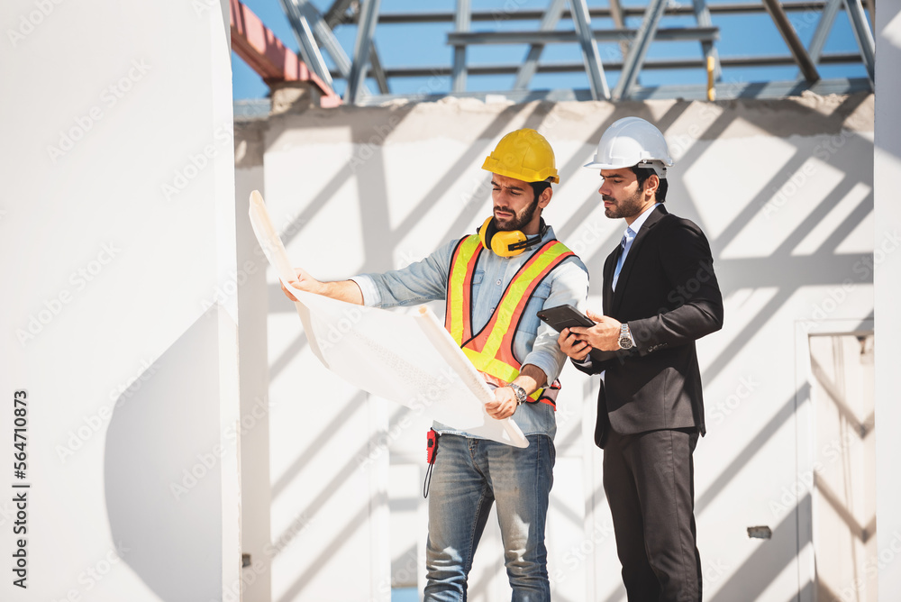 Teamwork men in construction site, Two civil engineer in safety helmet hard hat using digital tablet and blueprint working while standing at factory. Teamwork men in construction site, Two civil engineer in safety helmet hard hat using digital tablet and blueprint working while standing at factory.