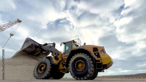 A bucket loader pulls up and dumps sand into a large pile