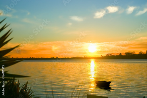 Small dinghy at anchor in silhouette back-lit by intense sunrise