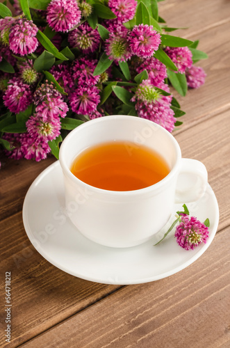 Healthy herbal tea with clover in a white cup on a brown wooden background with a bouquet of clover
