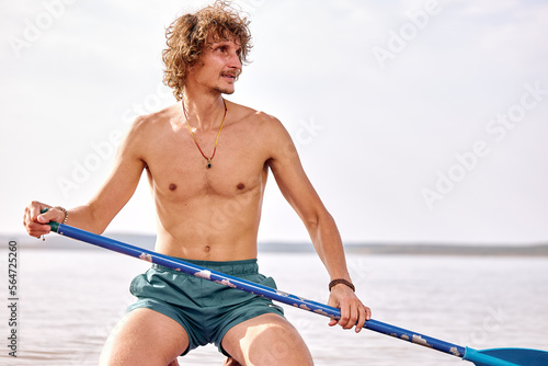 Curly athlete surfing in lake, caucasian Surfer young man performing subsurfing alone, sitting on board. Extreme sport, travel, healthy lifestyle, adventure and vacation concept
