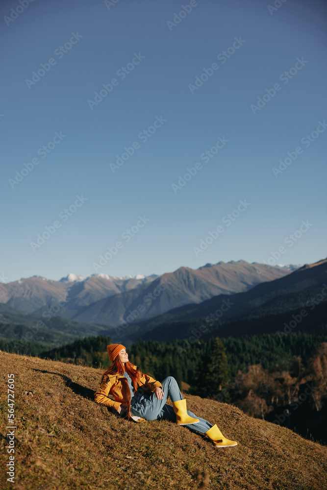 Woman full-length sitting resting on a hill and looking at the mountains in a yellow raincoat and jeans happy camping trip in the winter, freedom lifestyle 