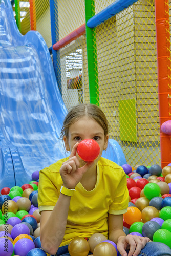 A funny girl is having fun playing with colorful balls in the game center and riding down a slide