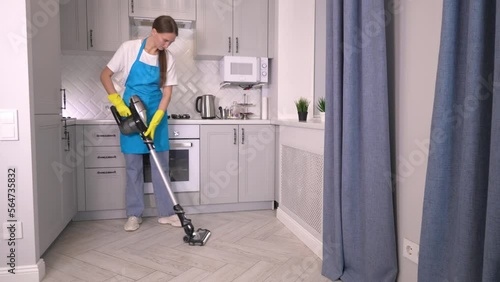 Caucasian maid cleaning of hotel room or apartment kitchen, . staff at maid's work, professional profession. Housekeeper wipes floor with cordless vertical vacuum cleaner at home. housewife. photo