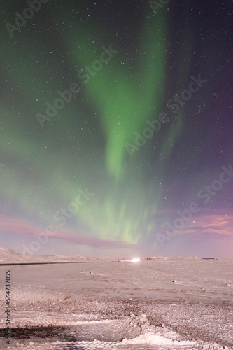 imagen nocturna de un paisaje nevado con una aurora boreal iluminando el cielo de color verde y las estrellas de fondo