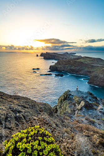 Woman enjoys panoramic view from a steep cliff over the seascape and along the rugged foothills of Madeira coast at sunrise. Ponta do Bode, Madeira Island, Portugal, Europe.