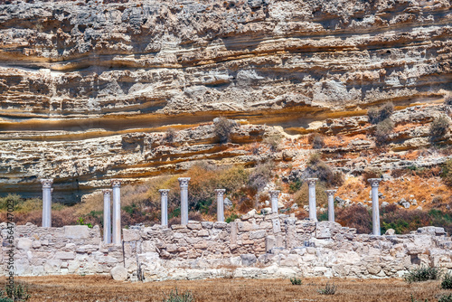 Ruins of the ancient city of Kourion. The columns are set against a rock with strange horizontal crevices and ancient artifacts.