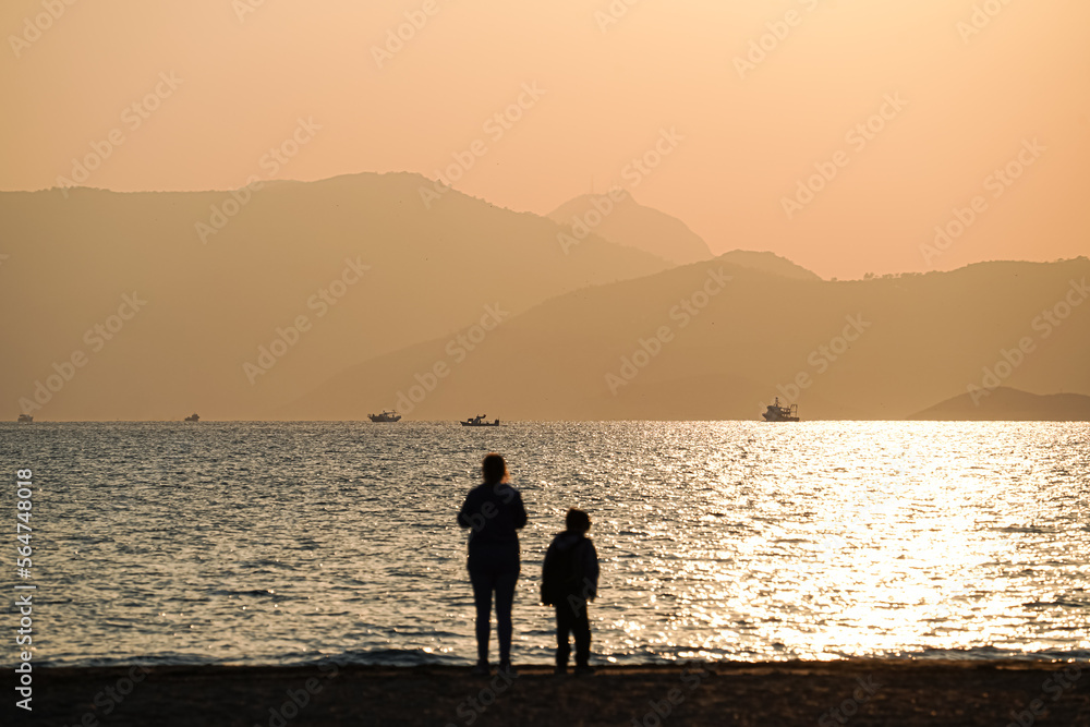 Woman and kid (mother and son) walking at the beach in windy winter beach, empty space, copy space Woman and kid (mother and son) walking at the beach in windy winter beach, empty space, copy space