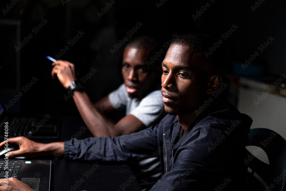 Two black males looking at computer screen in dark room