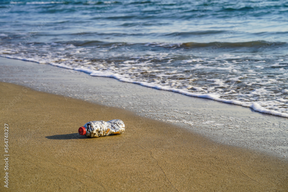 Obraz premium A bottle of cigarette butt stub on the clean beach sand near mediterranean sea and ocean, to pay attention to environmental pollution, global warming and warning, no smoking area