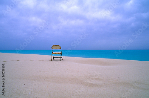 A folding chair sits on a deserted beach overlooking a lagoon. photo