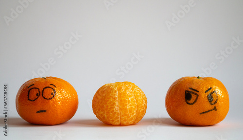 Two whole tangerines look with suspicion and fear at a peeled mandarine. Three orange cheerful fruits expressing emotions. Funny faces. Space for text