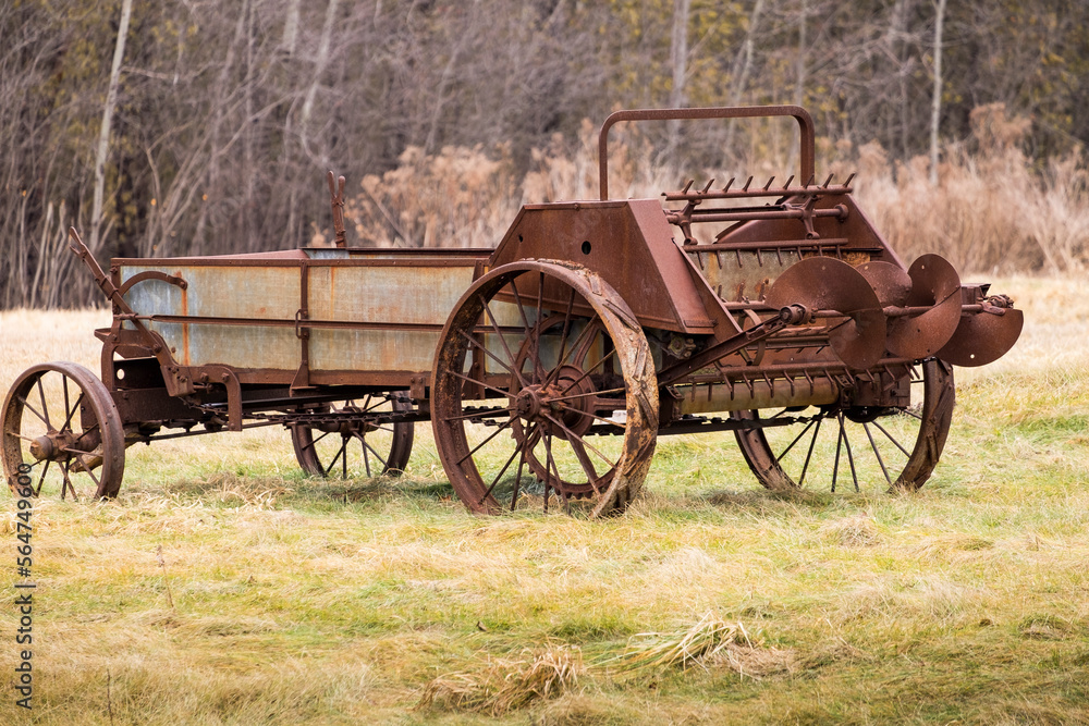 An old rusty manure spreader with iron wheels in a field in rural Ontario Canada.
