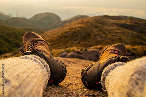  Man sitting on the rock, with his hiking boots, with a beautiful view behind. In the Serra dos Orgãos park in Rio de Janeiro Brazil
