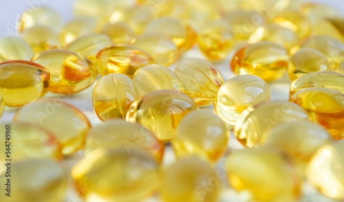 Yellow capsules with fish oil scattered on a white background. Omega-3 and vitamin D tablets.