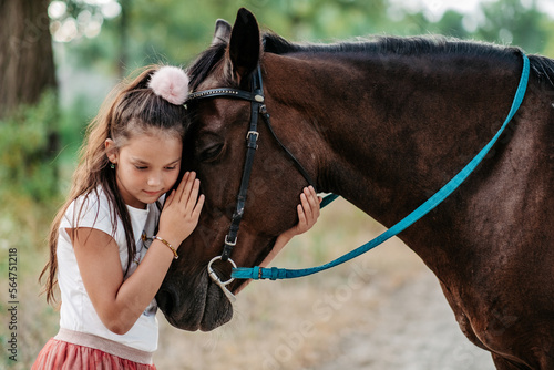 Cute little girl stroking a horse's head on a farm in the countryside in summer. Love for horses.