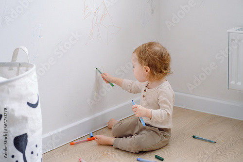Toddler scribbling on white wall at home. Little kid drawing on walls by colored markers. Art therapy, normal development. 