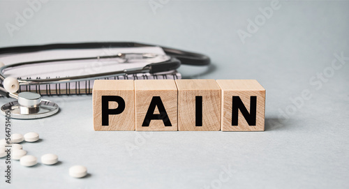 PAIN inscription on wooden cubes isolated on white background, medicine concept. Nearby on the table are a stethoscope and pills.