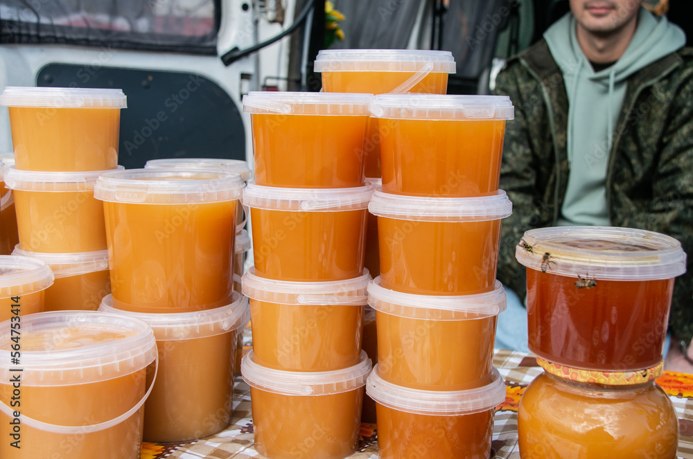 Sale of honey in transparent plastic jars at the agricultural market. Sale of beekeeping products. Sweet food. Close-up