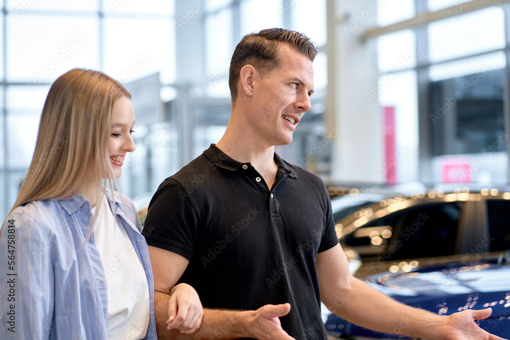 Happy young caucasian family dreaming of buying purchasing new expensive car, checking auto options, talking, discussing, trying it on at dealer shop store. clients customers in dealershop Happy young caucasian family dreaming of buying purchasing new expensive car, checking auto options, talking, discussing, trying it on at dealer shop store. clients customers in dealershop