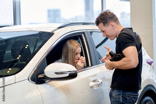 lovely caucasian blonde woman begs boyfriend to buy auto in car showroom. In Auto In Dealership. cars, automobiles, transport, family relationships concept. female want to get new auto by husband