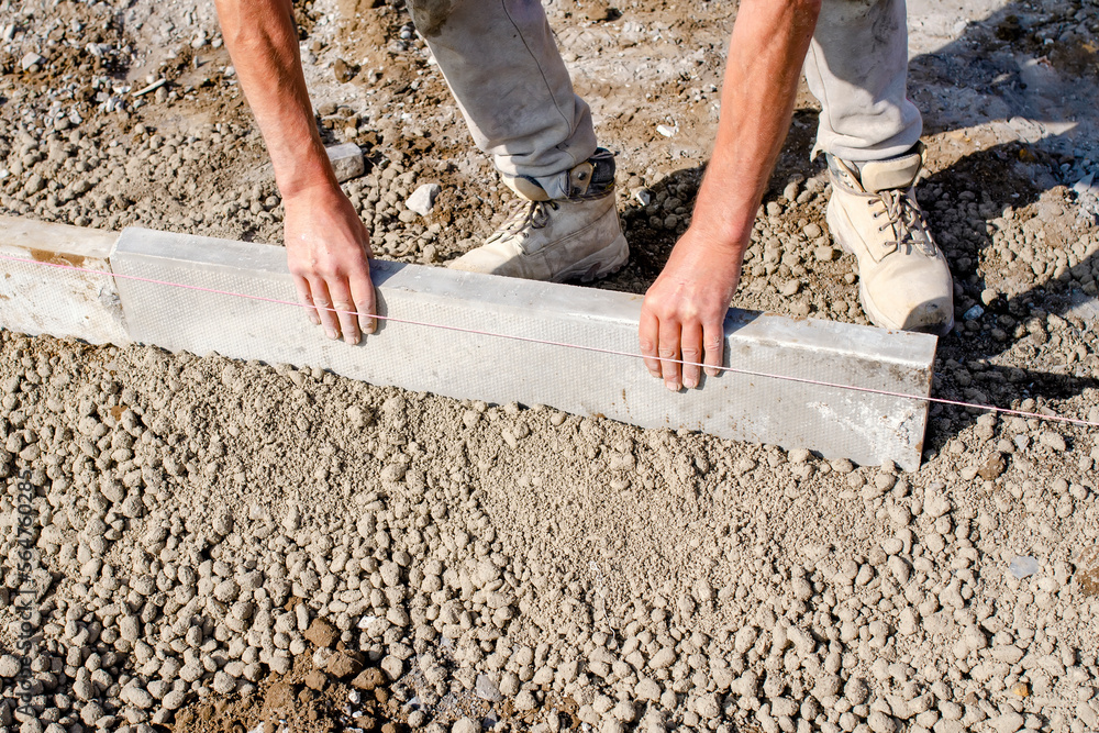 Builder placing edging pin kerb on semi-dry concrete using a