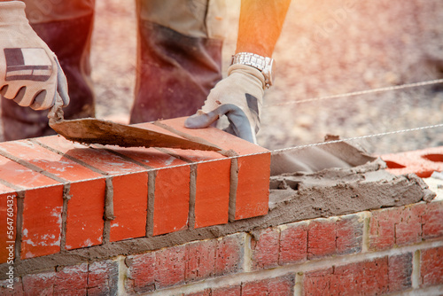 Industrial bricklayer laying bricks on cement mix on construction site photo
