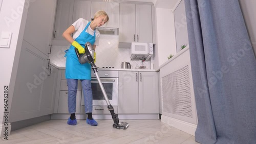 Caucasian maid cleaning of hotel room or apartment kitchen, . staff at maid's work, professional profession. Housekeeper wipes floor with cordless vertical vacuum cleaner at home. housewife. photo