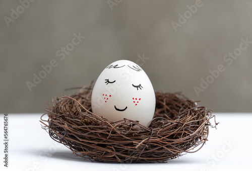 Happy Easter. One white Easter egg in a wicker wooden nest on white table. View is direct. Stylish spring template with copy space