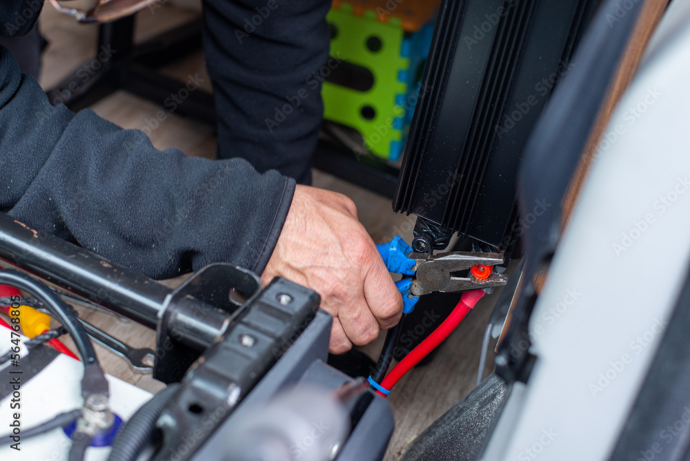 man hand servicing vehicle, tightening battery terminal with tool in hand.