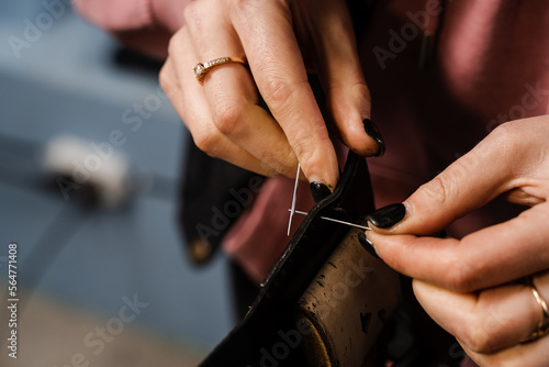 Craftsman sews genuine leather using needle and thread for creation natural leather products. Equipment for genuine leather production in workshop. Process of stitching genuine leather.