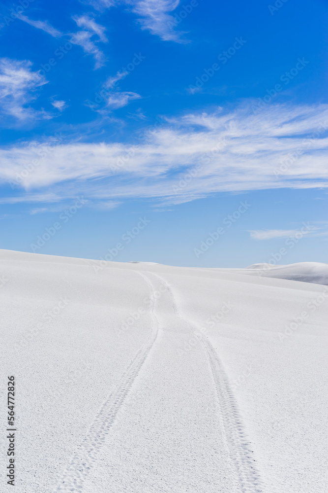 Tire tracks on white sand dunes against blue sky during sunny day Tire tracks on white sand dunes against blue sky during sunny day