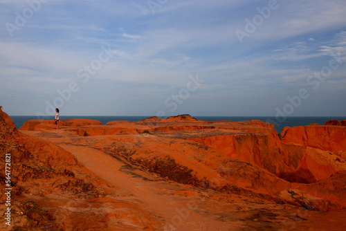 Distant view of woman standing on cliff by sea against sky during sunset photo