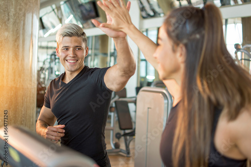 Cheerful couple doing cardio exercises on a treadmill and giving high-five to each other. Young happy couple running together in gym.