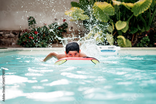 Handsome and dark-haired boy playing with a body surf board in the pool