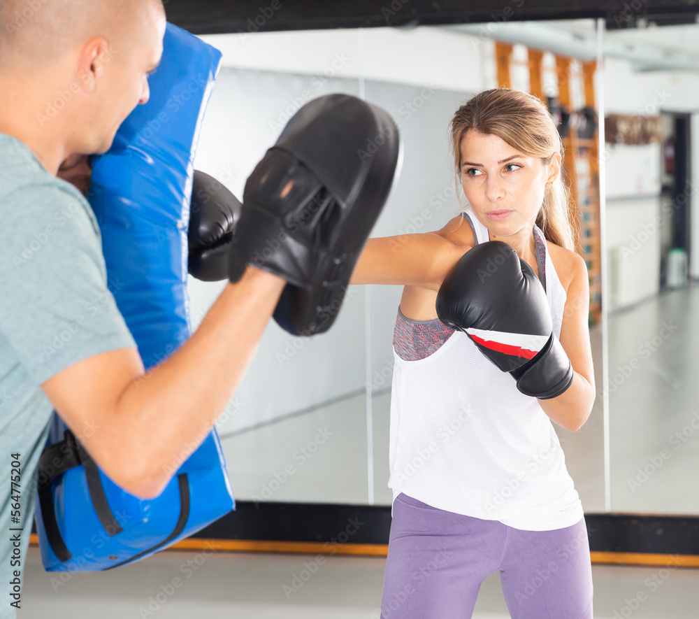 Adult man is training with woman and punching gloves in box gym